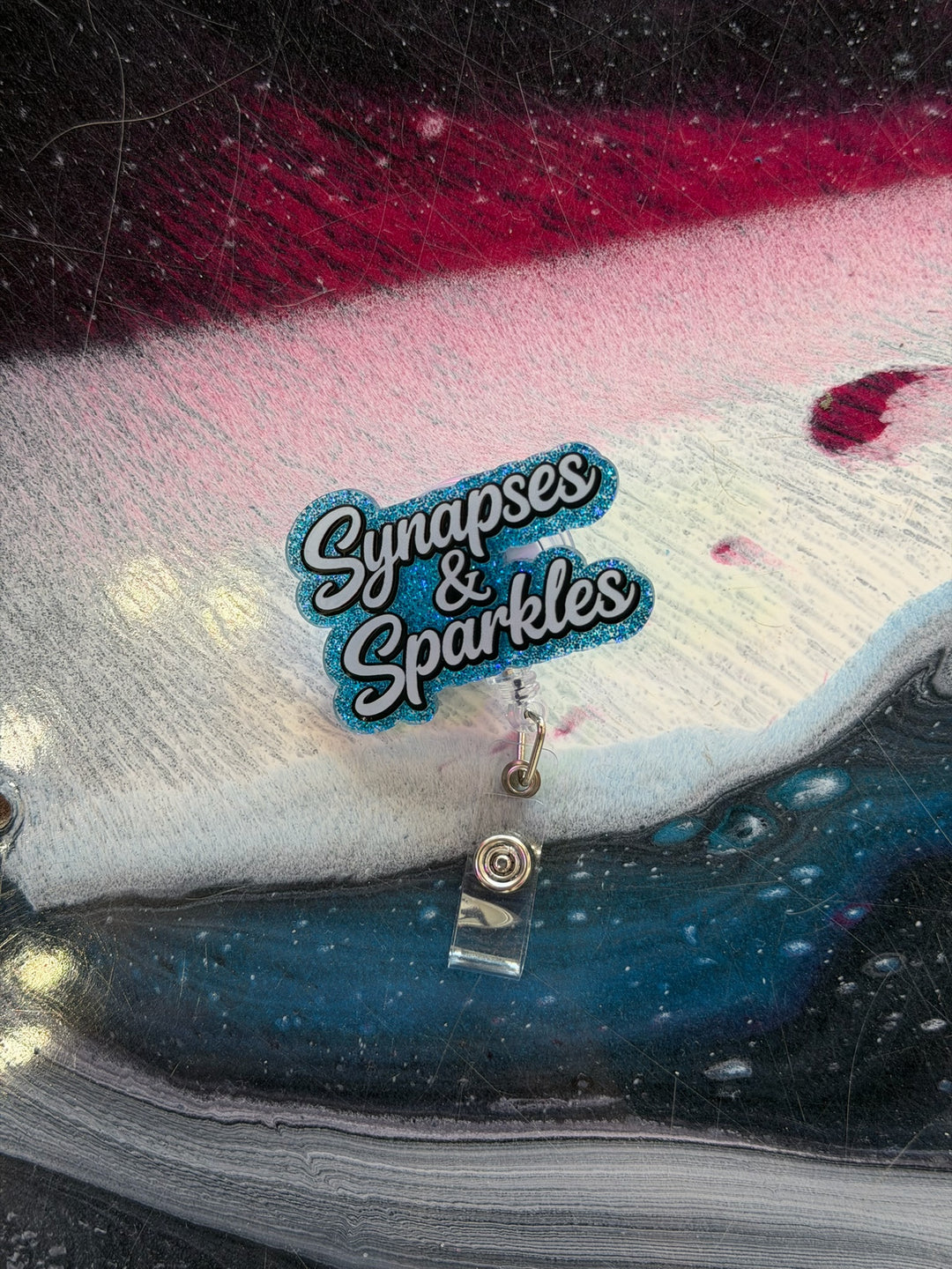 Colorful badge holder with 'Synapses & Sparkles' logo on a dark background