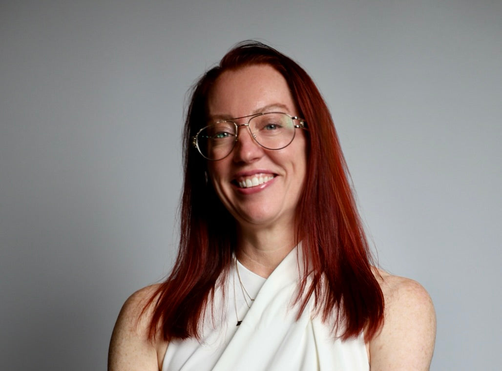 Dr. Betsy Grunch (aka Ladyspinedoc) wearing glasses smiling against a gray background