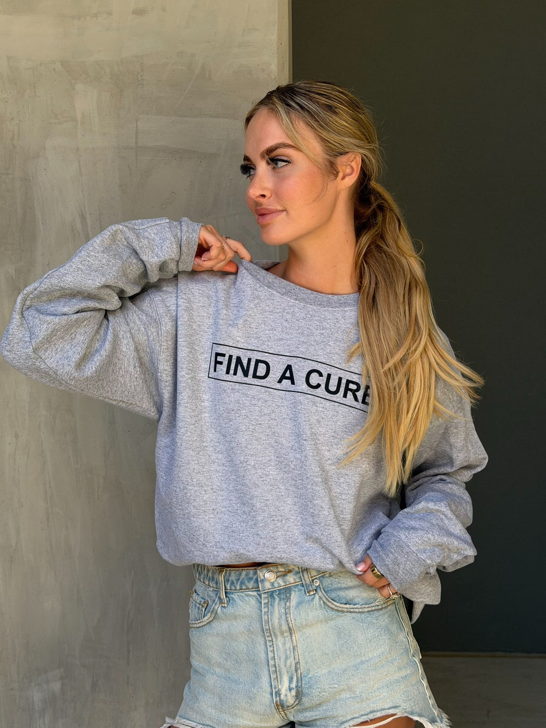 Woman wearing a gray sweatshirt with 'FIND A CURE' text against a neutral background