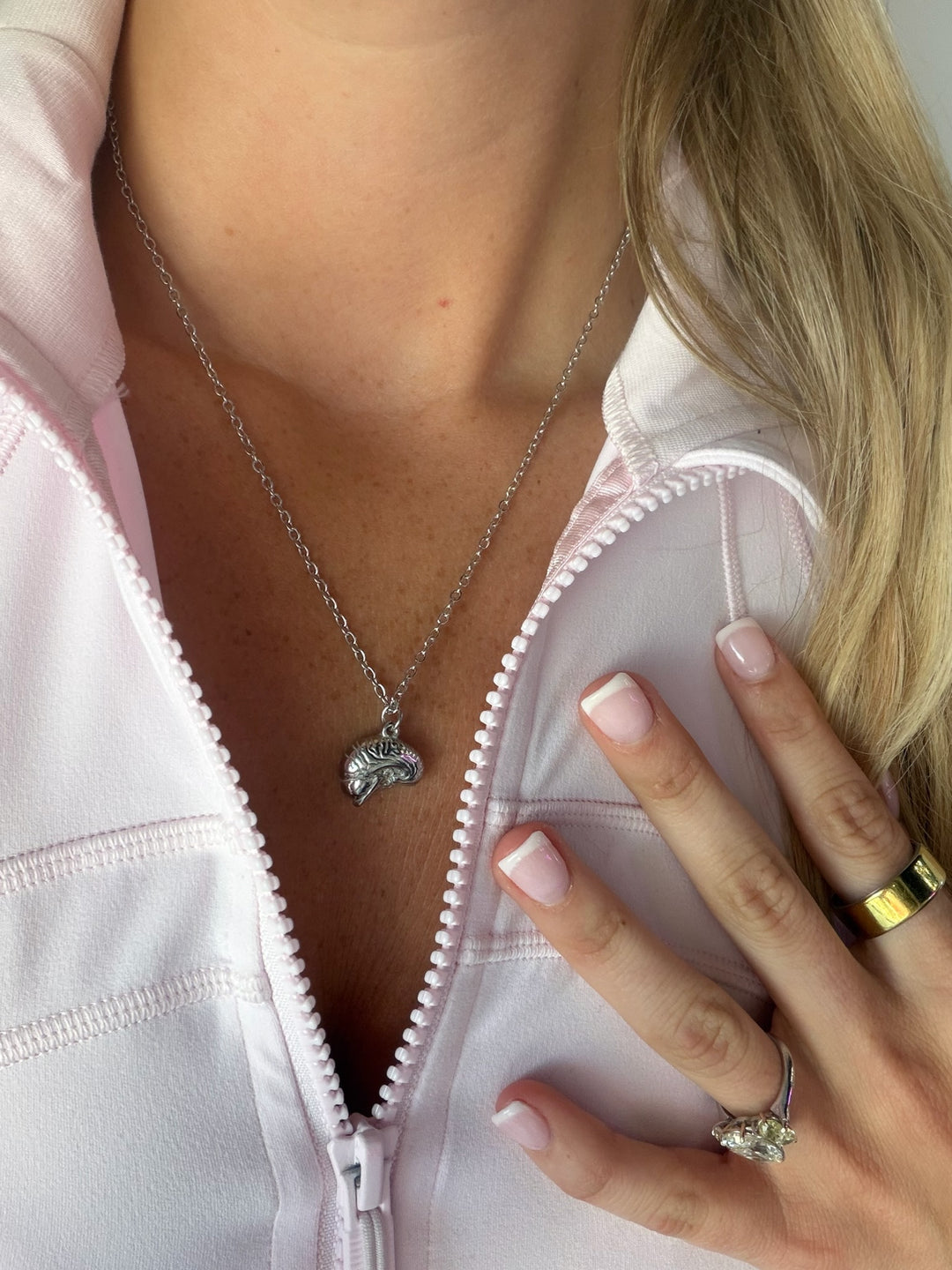 Close-up of a necklace with a brain pendant worn by a person in a pink jacket.