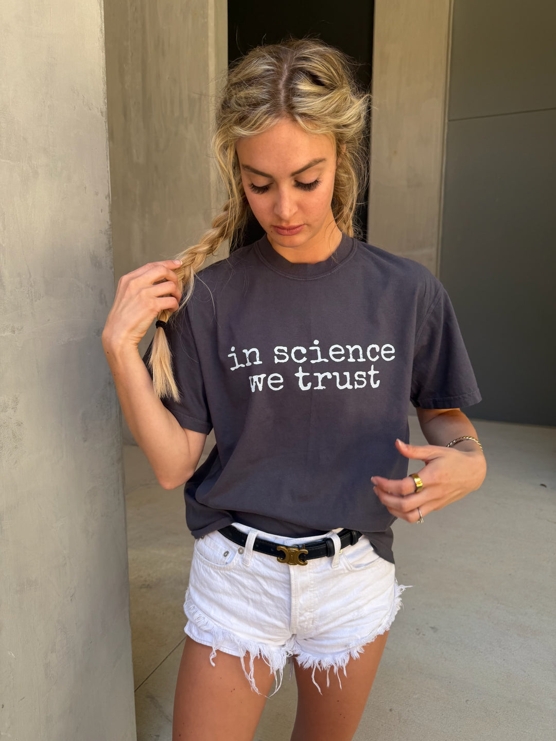 Woman wearing a dark gray t-shirt with 'in science we trust' text outdoors.