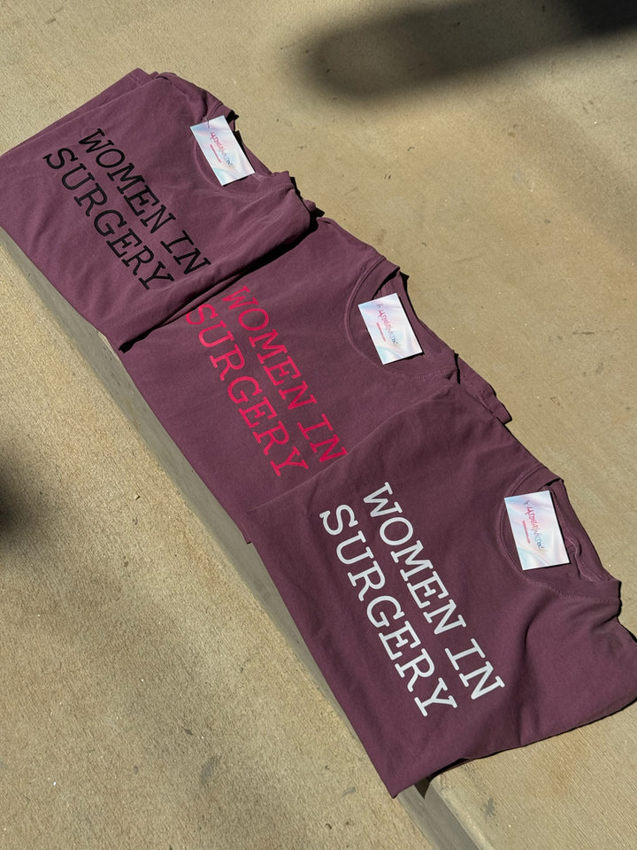 Maroon t-shirts with 'Women in Surgery' text on a concrete surface