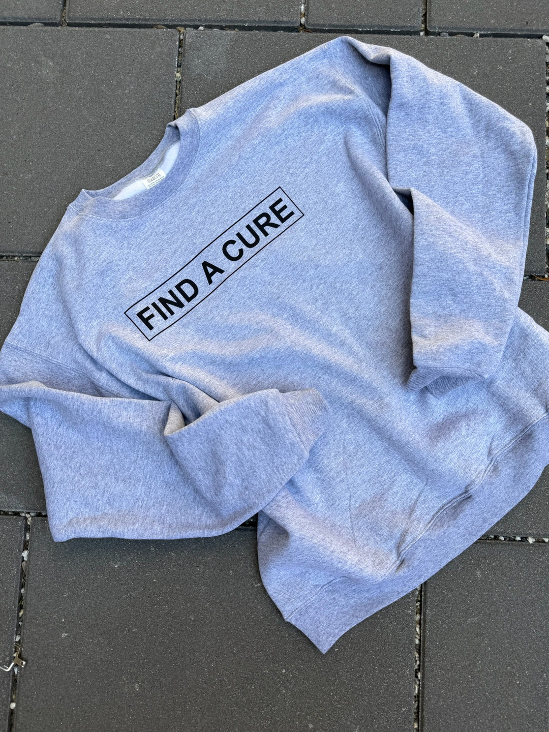 Gray sweatshirt with 'FIND A CURE' text on a dark tiled floor