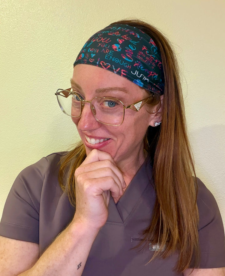 Ladyspinedoc wearing a colorful JUNK headband with text, glasses, and scrubs against a plain background