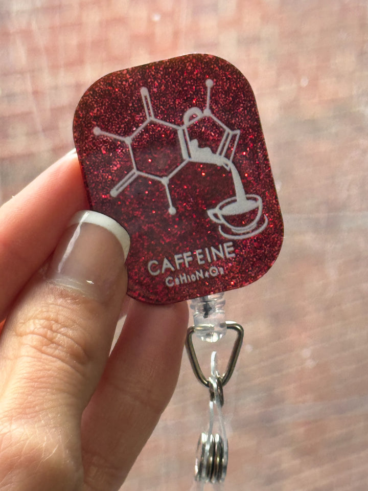 Woman holding Ladyspinedoc Red Sparkly Enerjava Badge Reel - Retractable with Alligator Clip and Caffeine Molecule Design on a dark red glitter background