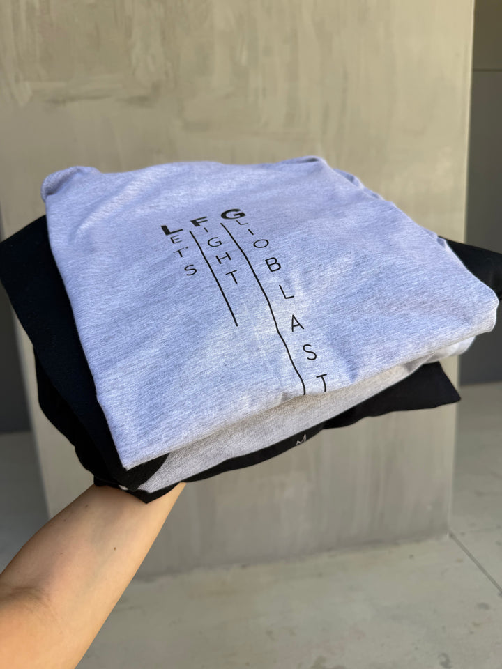 Pile of black and gray Let's Fight Glioblastoma shirts held by a hand against a neutral background