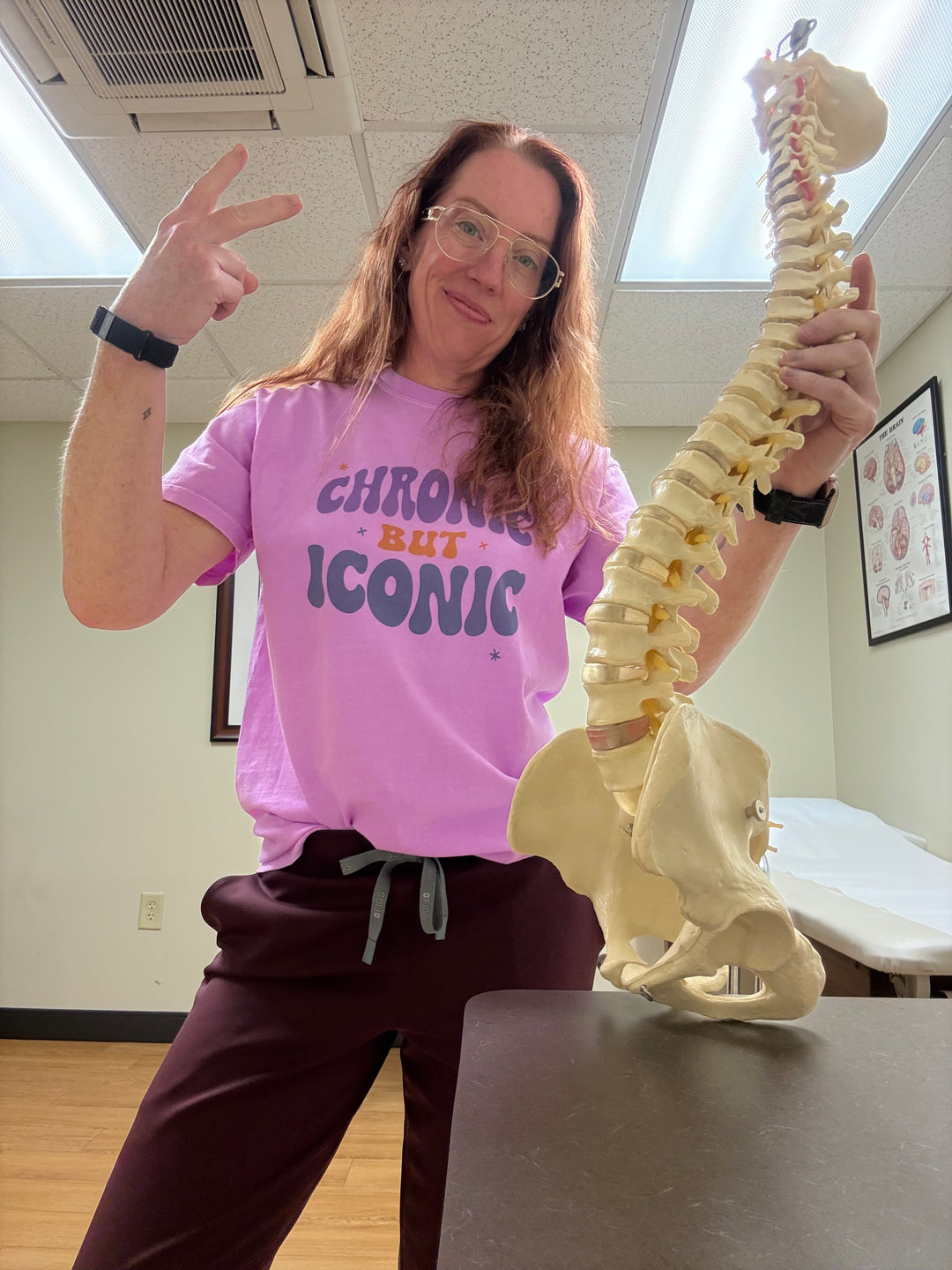 Dr. Betsy Grunch holding a model of a spine and wearing her Chronic But Iconic t-shirt