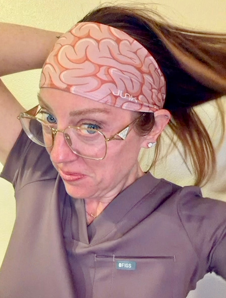 Ladyspinedoc wearing her JUNK Brand headband with a brain design and glasses, against a neutral background