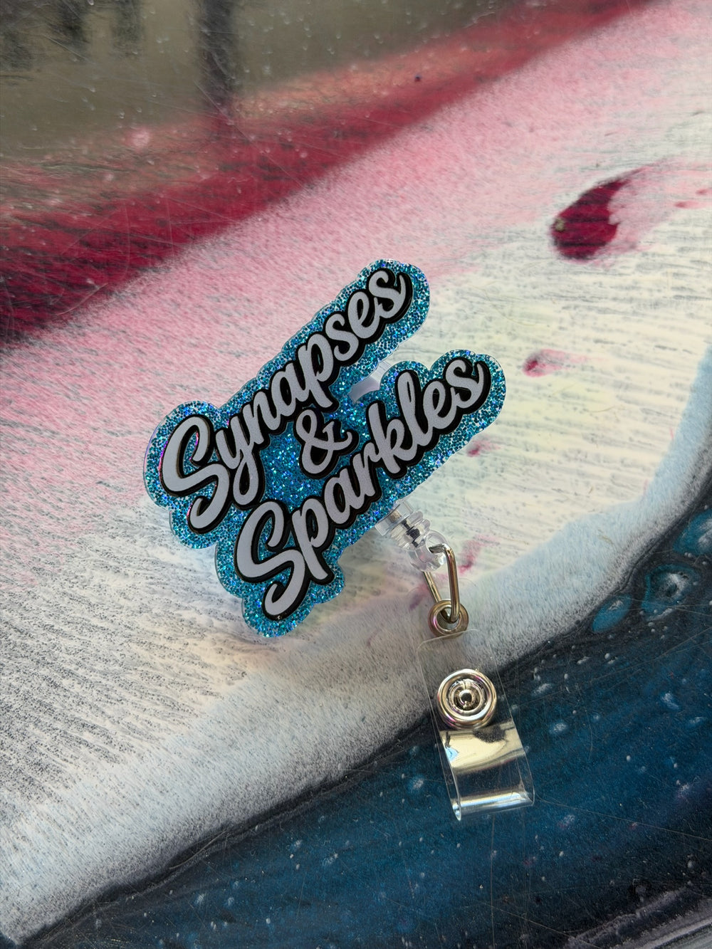 Badge holder with 'Synapses & Sparkles' text on a textured surface