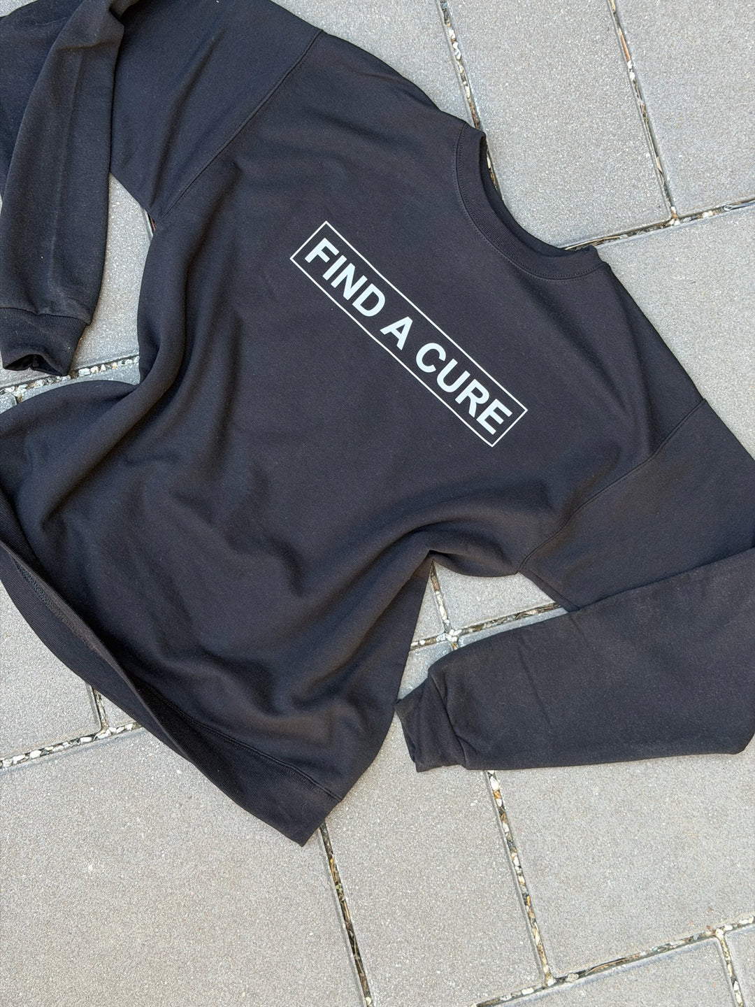 Black sweatshirt with 'Find a Cure' text on a tiled floor
