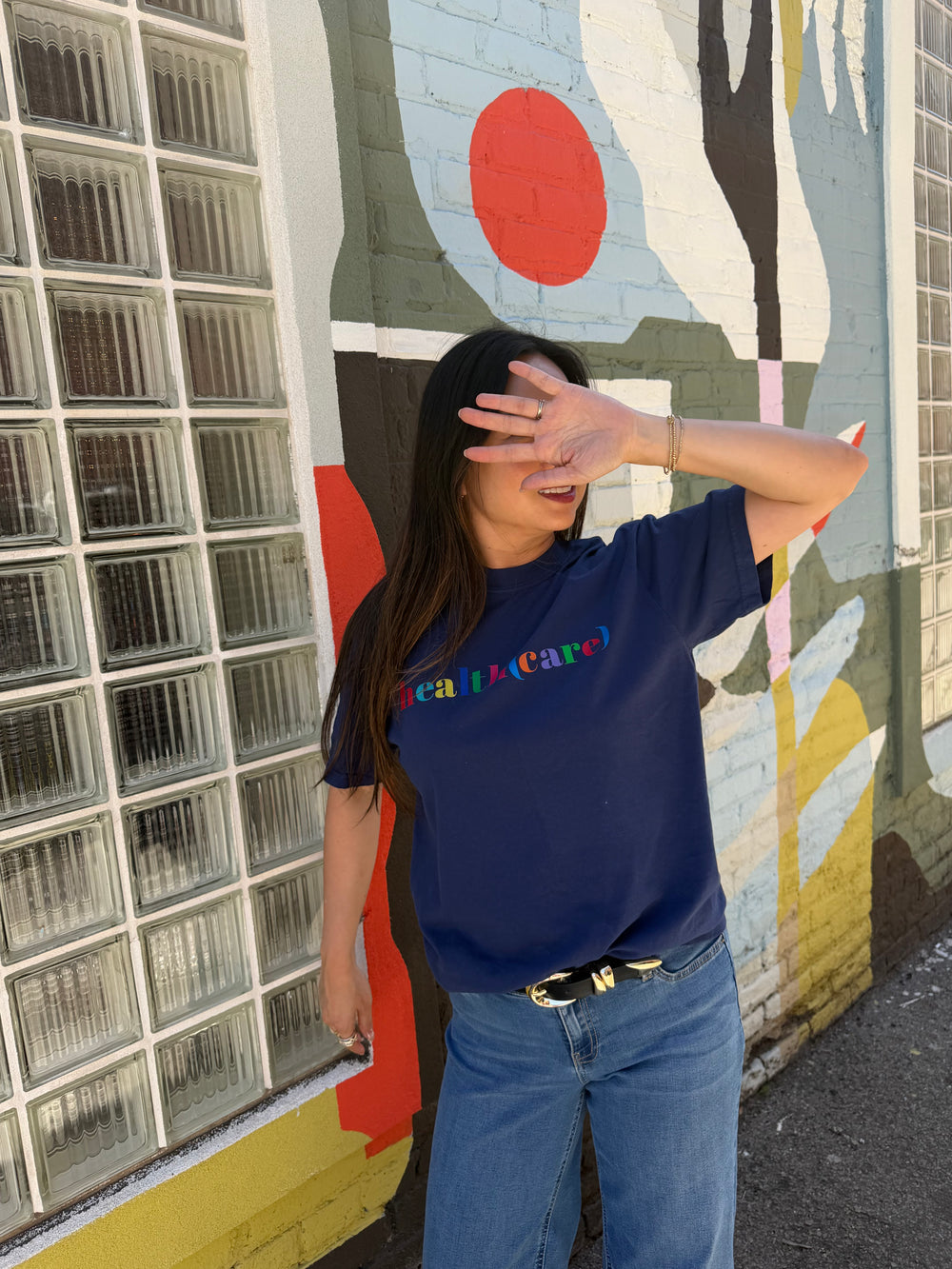Person wearing a blue health(care) tee outside next to a wall mural