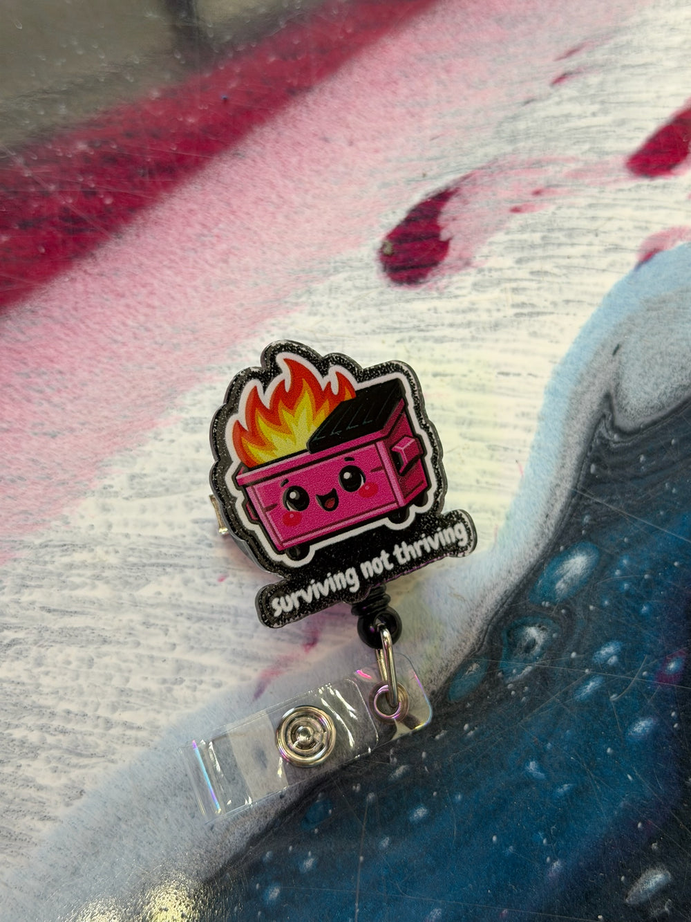Badge holder with a cartoon-style dumpster fire design on a textured surface