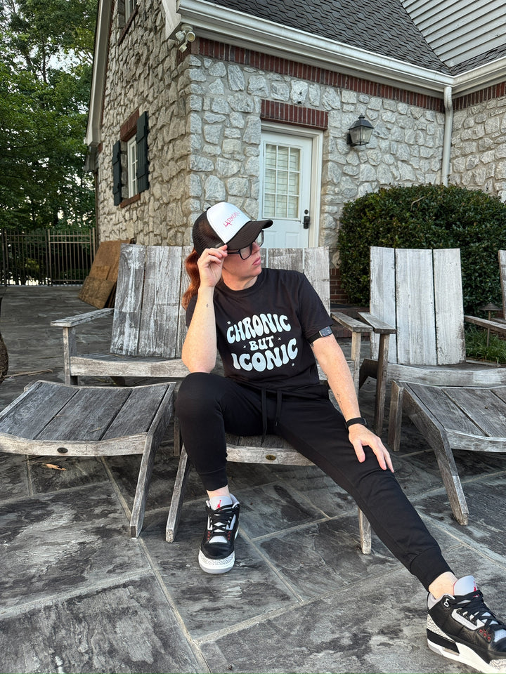 Dr. Betsy Grunch sitting on a wooden chair outdoors wearing her black Chronic but Iconic t-shirt.