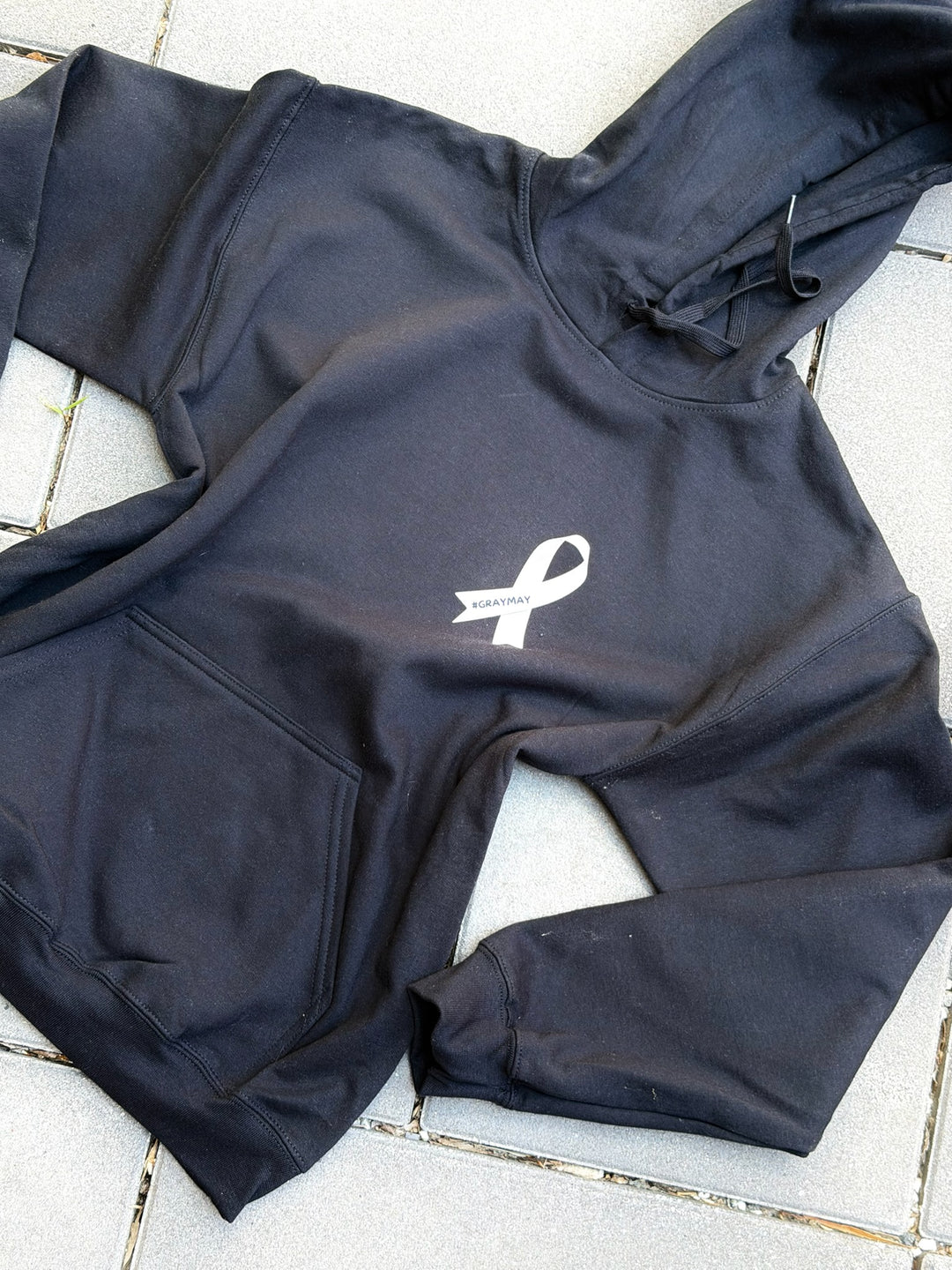 Black hoodie with a gray #GRAYMAY ribbon logo on a light gray tiled floor