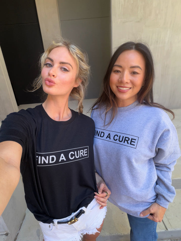 Two women wearing shirts with 'Find a Cure' text, standing outdoors.