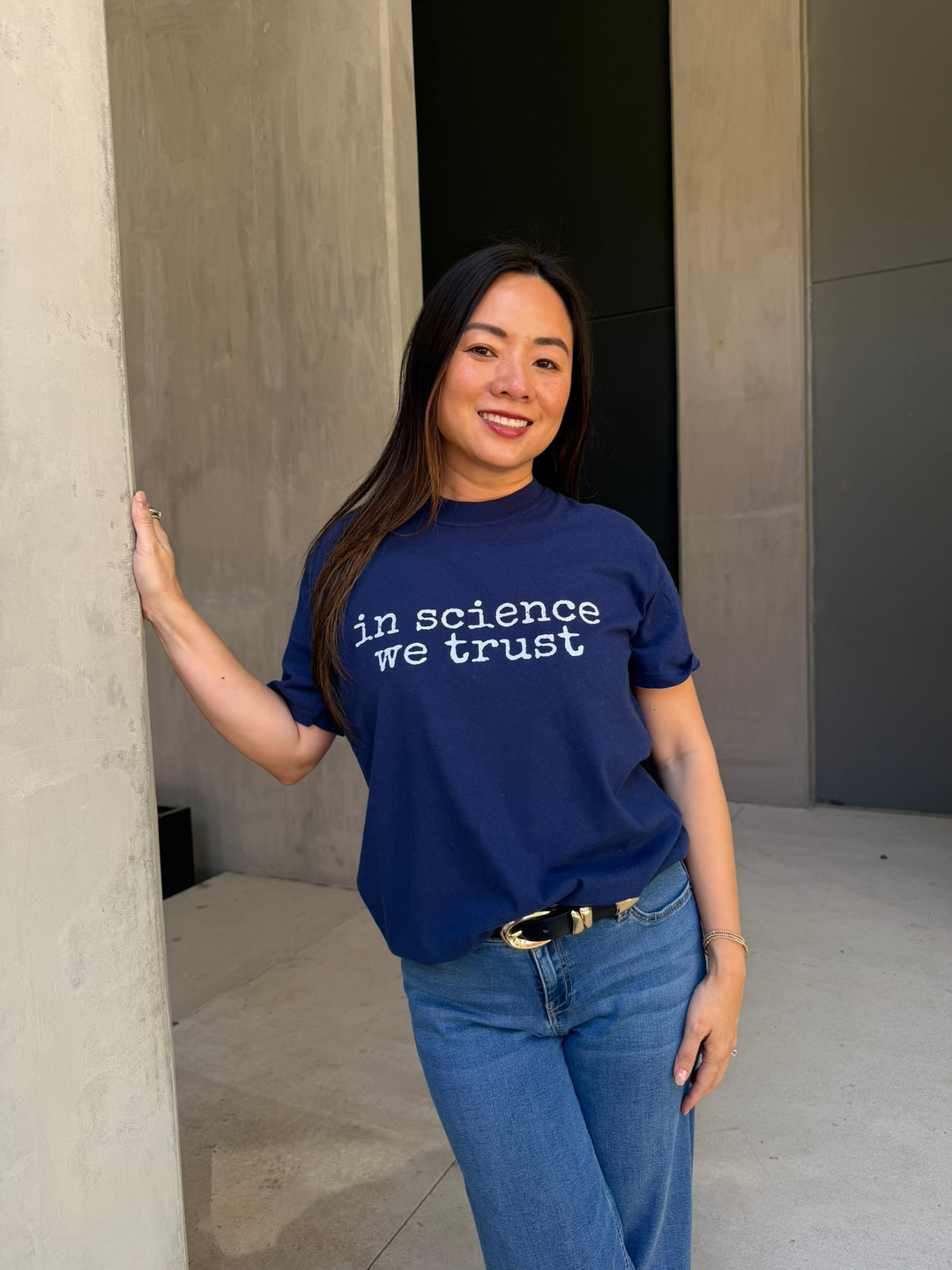 Person wearing a blue t-shirt with 'in science we trust' text, standing against a neutral wall.