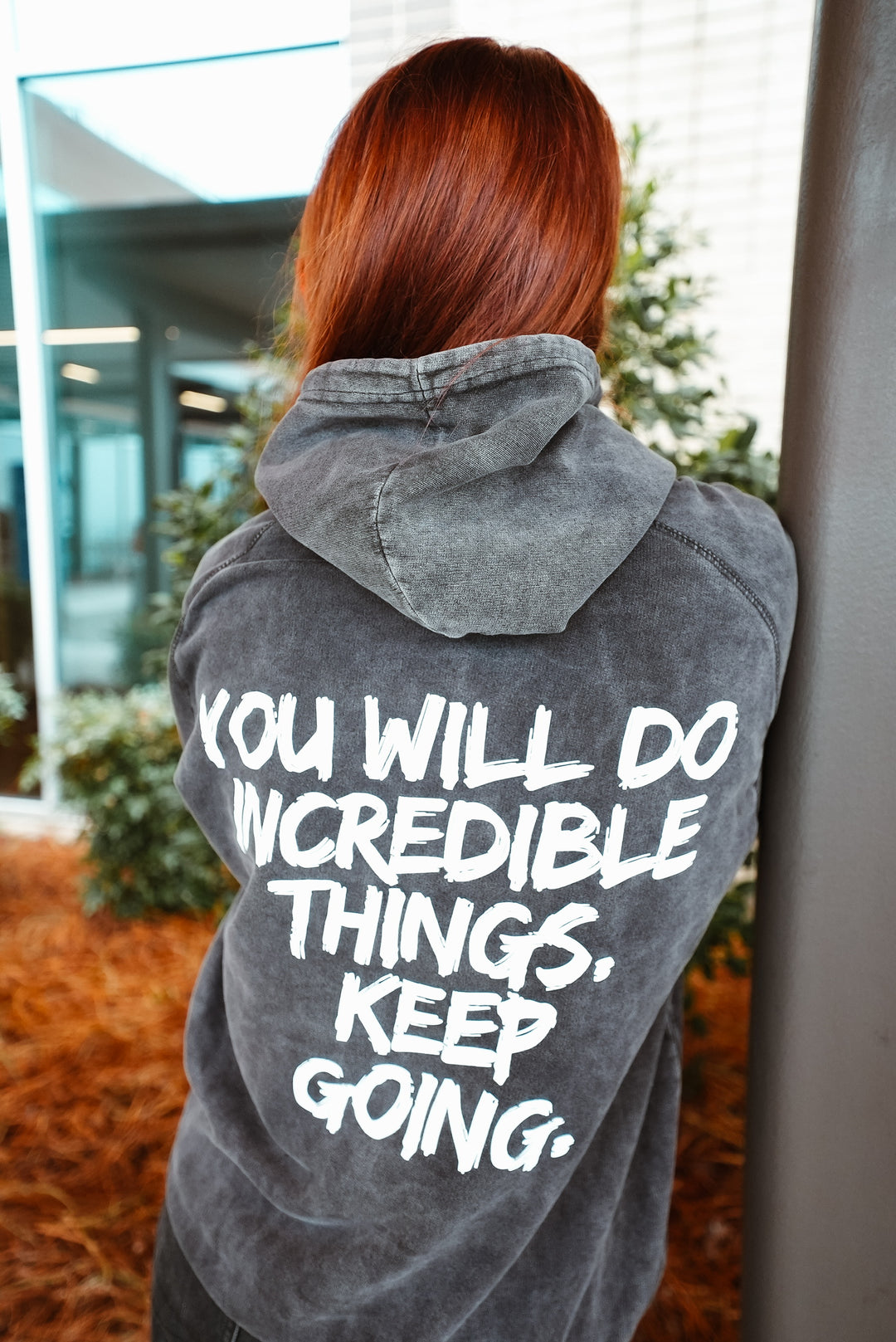 Ladyspinedo wearing a hoodie with motivational text on the back, standing indoors.