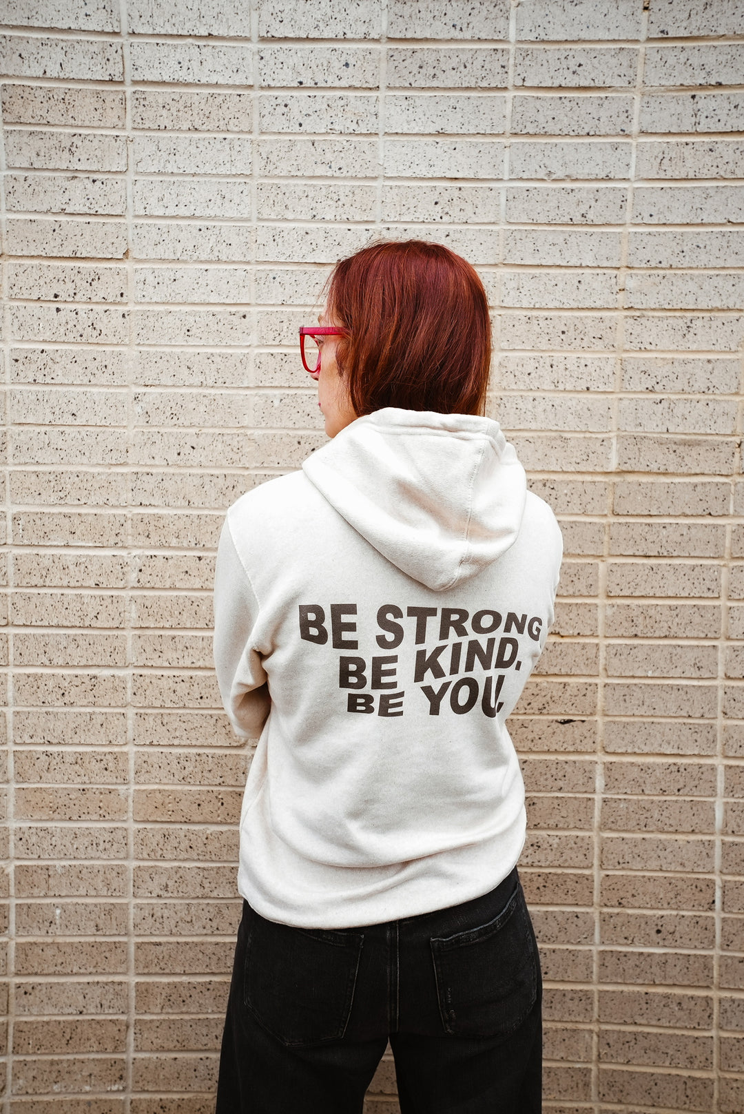 Ladyspinedoc wearing a white hoodie with motivational text against a brick wall