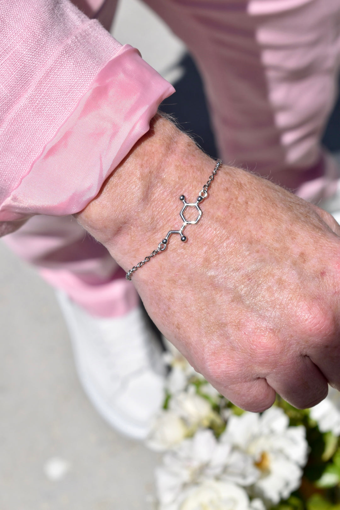 Close-up of a Ladyspinedoc's hand wearing a silver bracelet with a noradrenaline molecular design, against a blurred background.