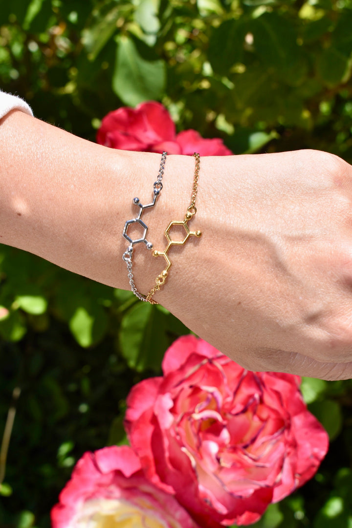 Two noradrenaline molecule bracelets  on a wrist against a floral background