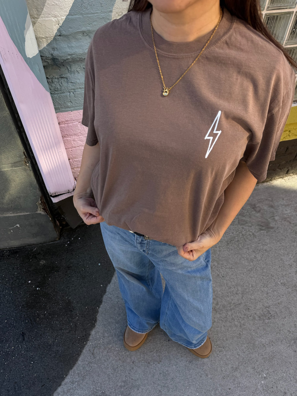 Person wearing a brown t-shirt with a white lightning bolt design and blue jeans.