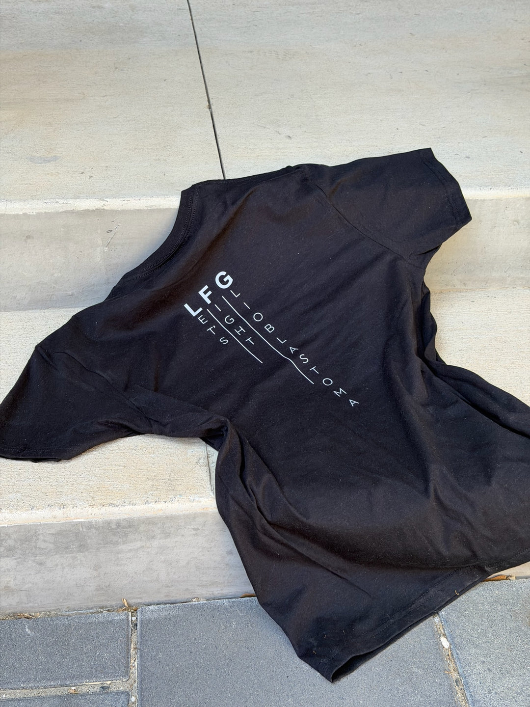 Black t-shirt with Let's Fight Glioblastoma text on a stone surface