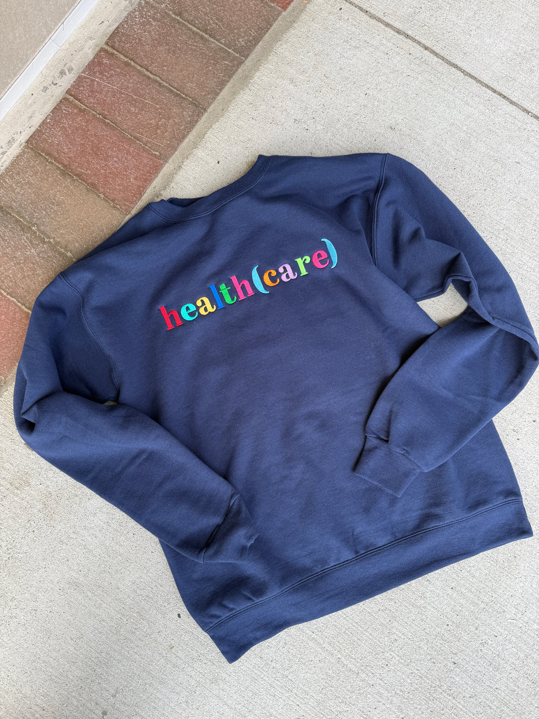 Blue sweatshirt with colorful health(care) text on a concrete surface