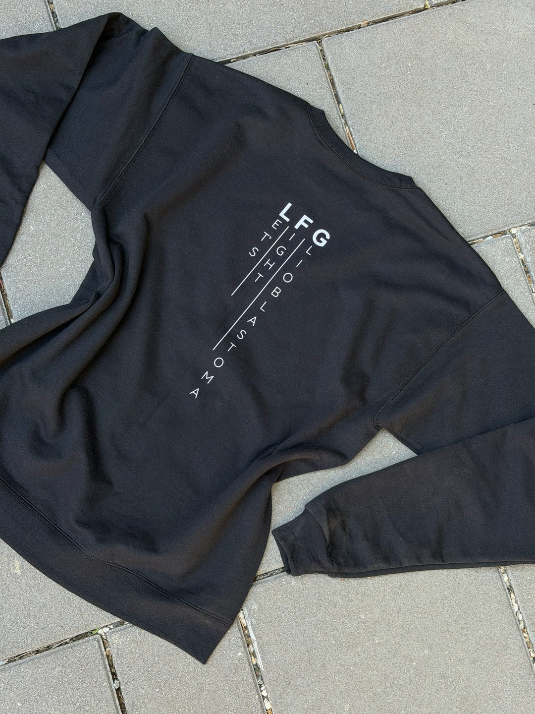 Black sweatshirt with Let's Fight Glioblastoma text on the back, laying on pavement