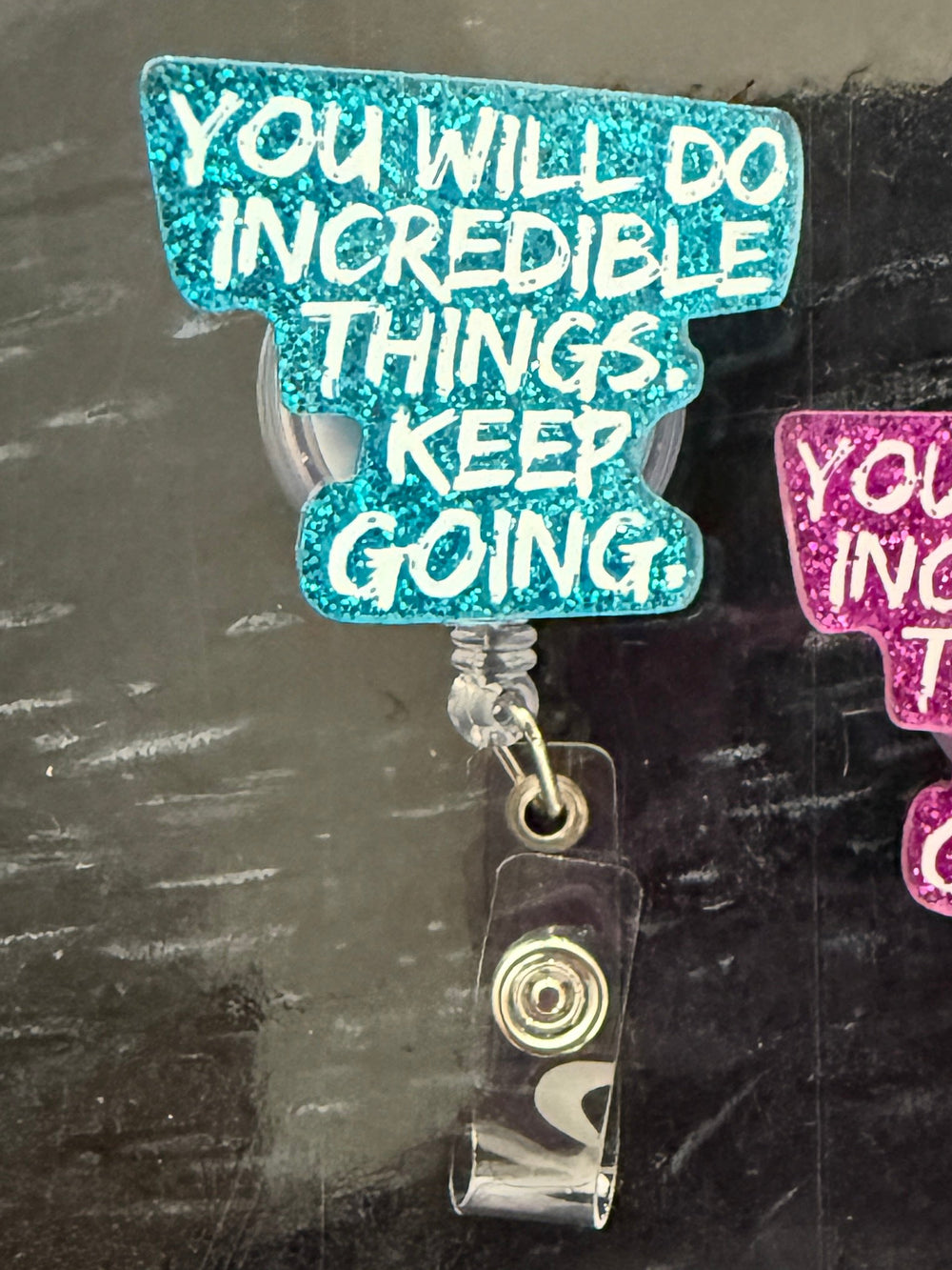 Two "You Will Do Incredible Things. Keep Going." motivational badge reel holders on a dark surface