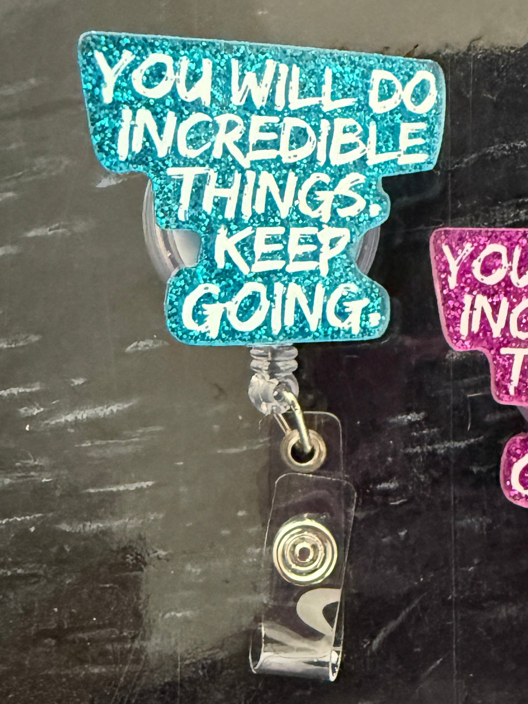 Two "You Will Do Incredible Things. Keep Going." motivational badge reel holders on a dark surface