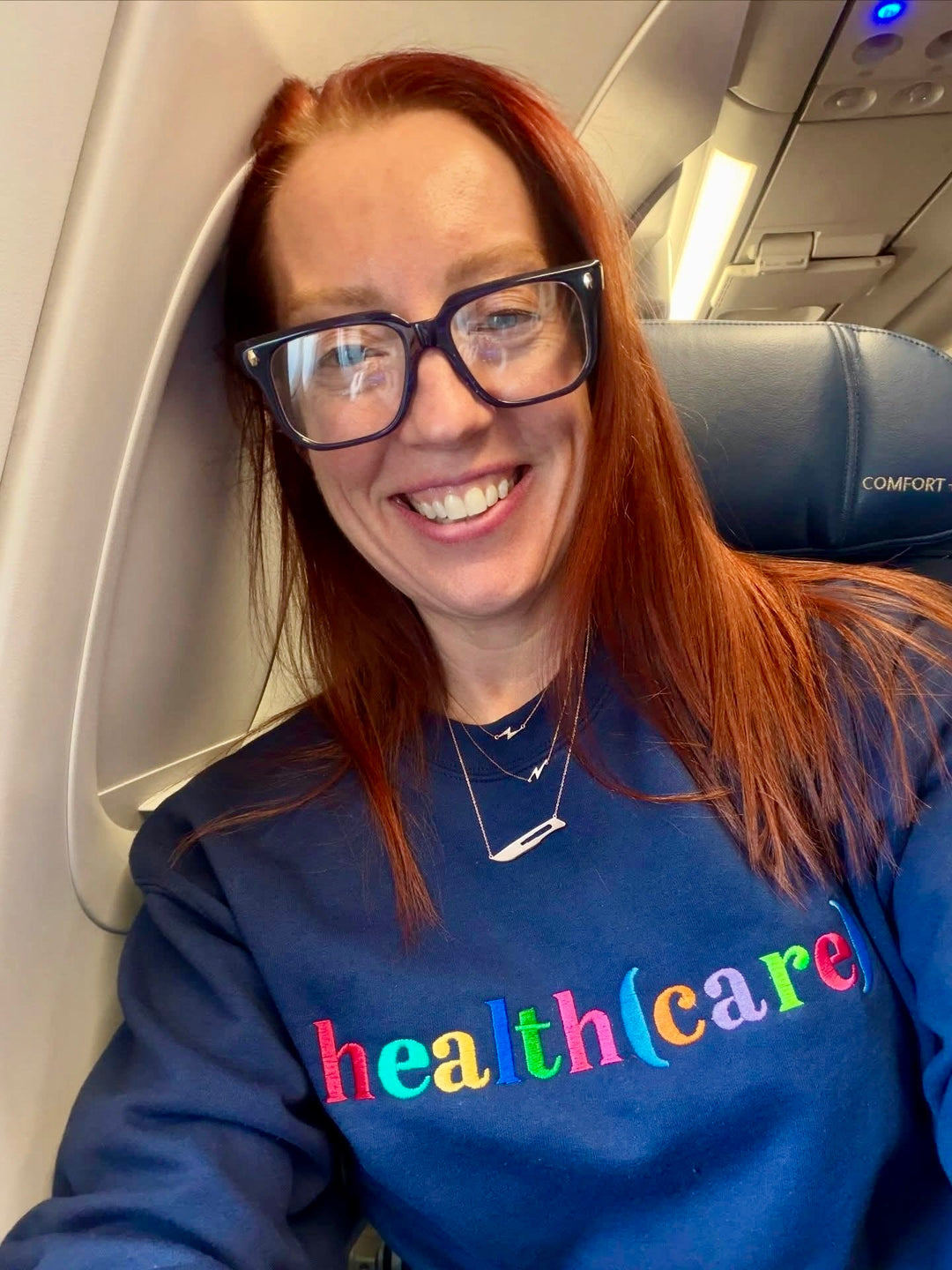 Ladyspinedoc wearing a blue sweatshirt with 'health(care)' on an airplane