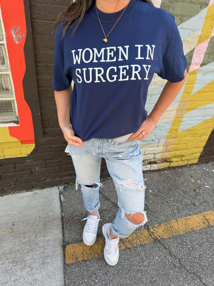 Person wearing a navy blue t-shirt with 'WOMEN IN SURGERY' text, standing in front of a colorful mural.