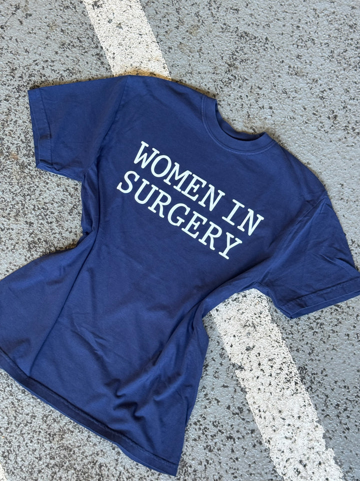 Blue t-shirt with 'WOMEN IN SURGERY' text on a concrete surface