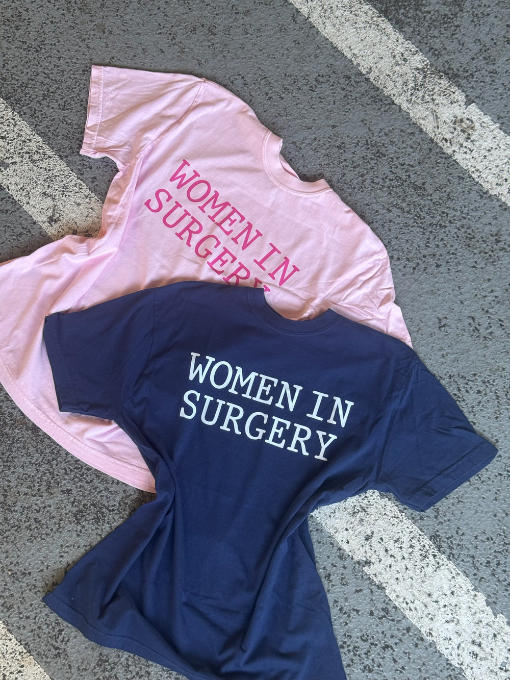 Pink and blue t-shirts with 'Women in Surgery' text on a textured surface