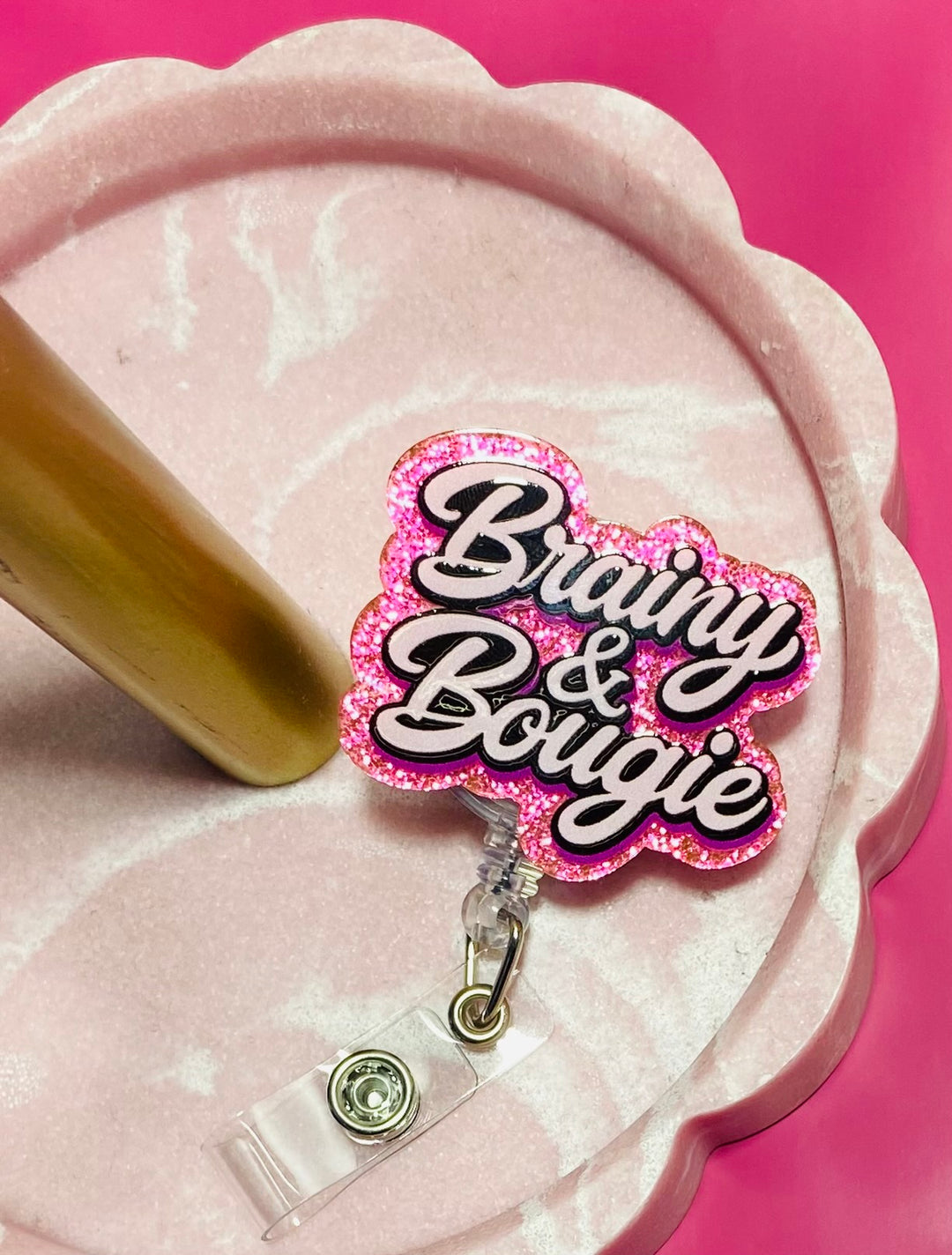 Pink and black 'Bravey & Bougie' badge holder with a pink glitter background