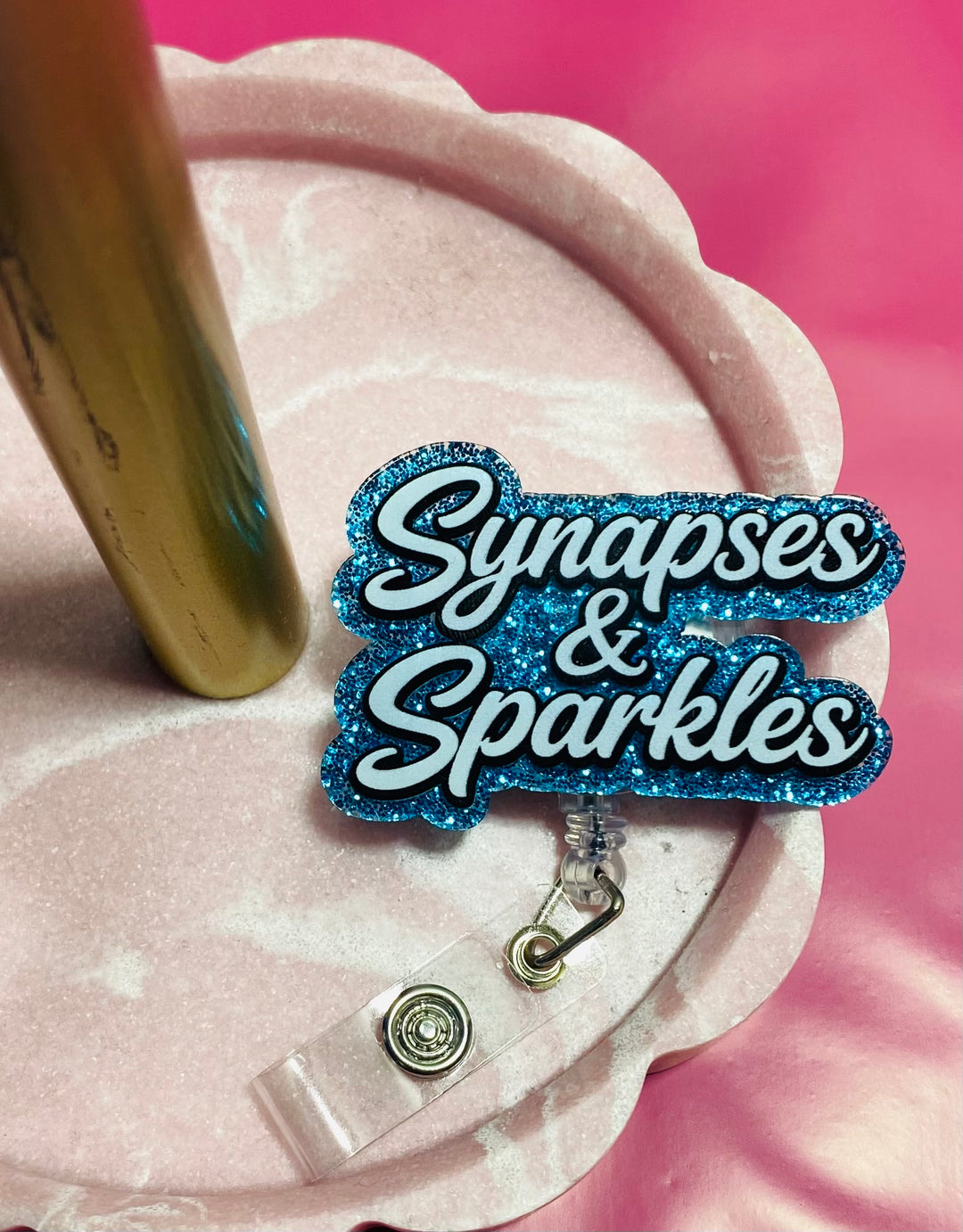 Blue sparkly badge holder with 'Synapses & Sparkles' text on a pink background