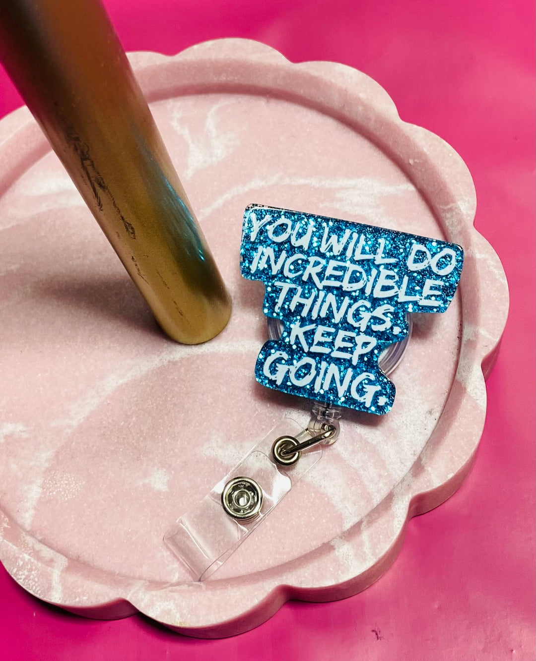Blue motivational badge reel on a pink stand with a pink background