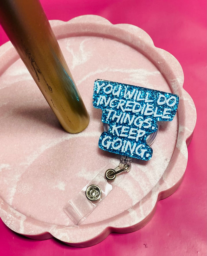Blue motivational badge reel on a pink stand with a pink background