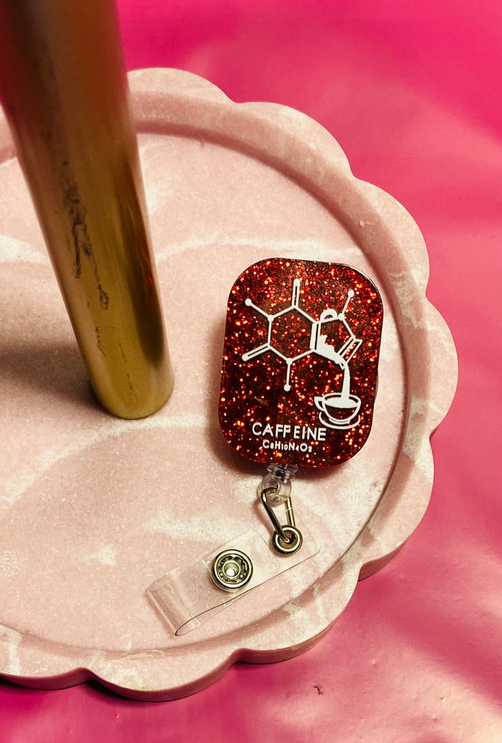 Red glittery badge reel with 'CAFFEINE' and molecular structure design on a pink background