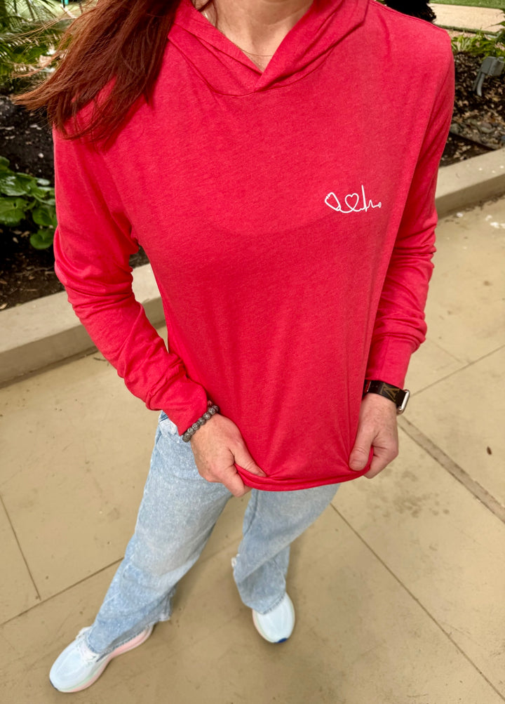 Dr. Betsy Grunch (Ladyspinedoc) wearing red long sleeve hoodie tee with Heart of Medicine logo, front view outdoors.