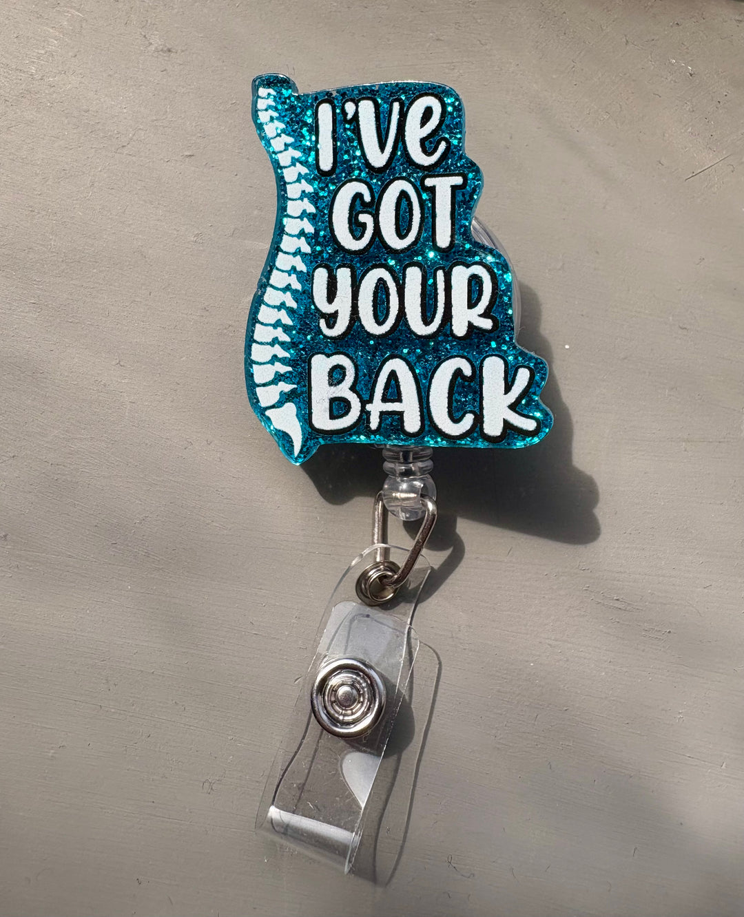 Blue glitter badge reel with a white spine graphic and the words “I’ve Got Your Back” in bold white lettering; features a clear retractable alligator clip.