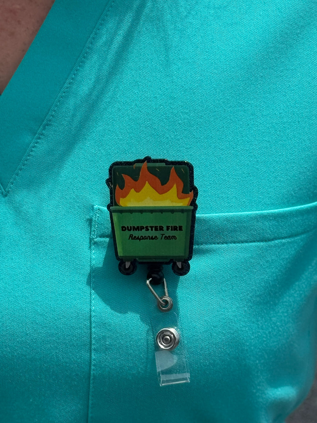 Close up of Ladyspinedoc Dumpster Fire Response Team Badge Reel clipped on front pocket of aqua scrub shirt