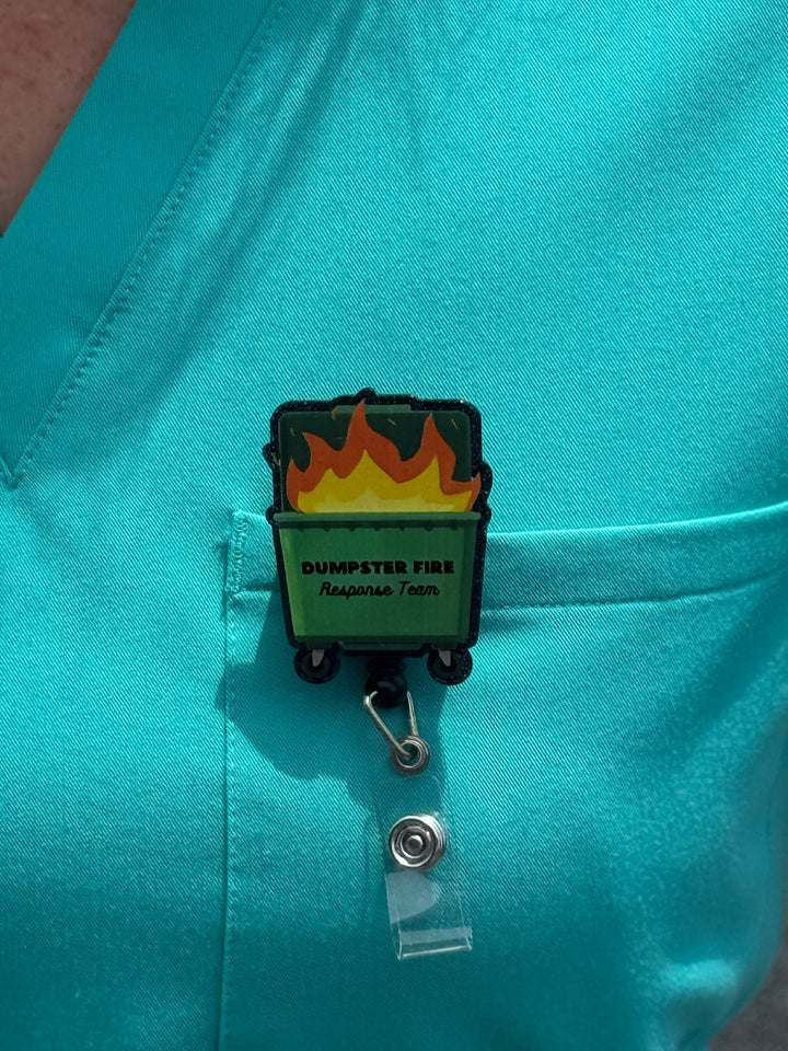 Close up of Ladyspinedoc Dumpster Fire Response Team Badge Reel clipped on front pocket of aqua scrub shirt