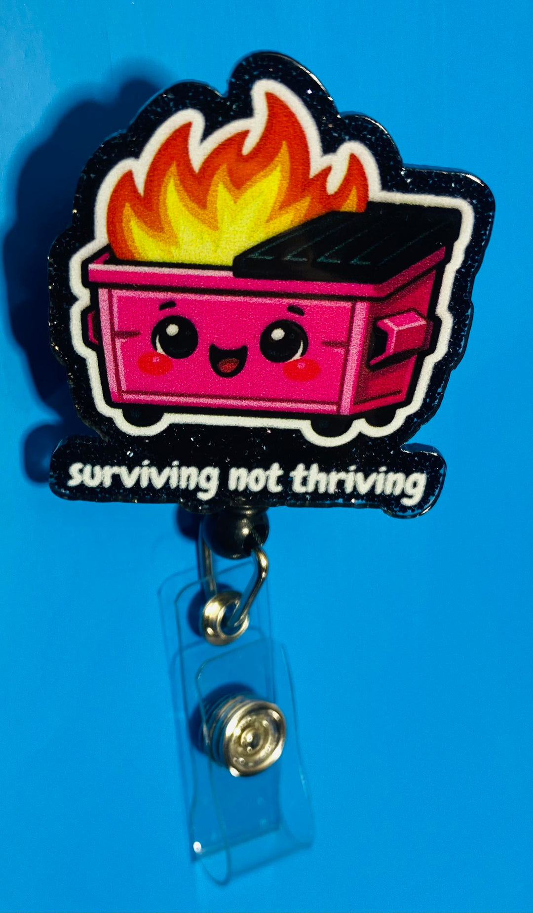 Pink cartoon-style dumpster with flames and 'surviving not thriving' text on a blue background