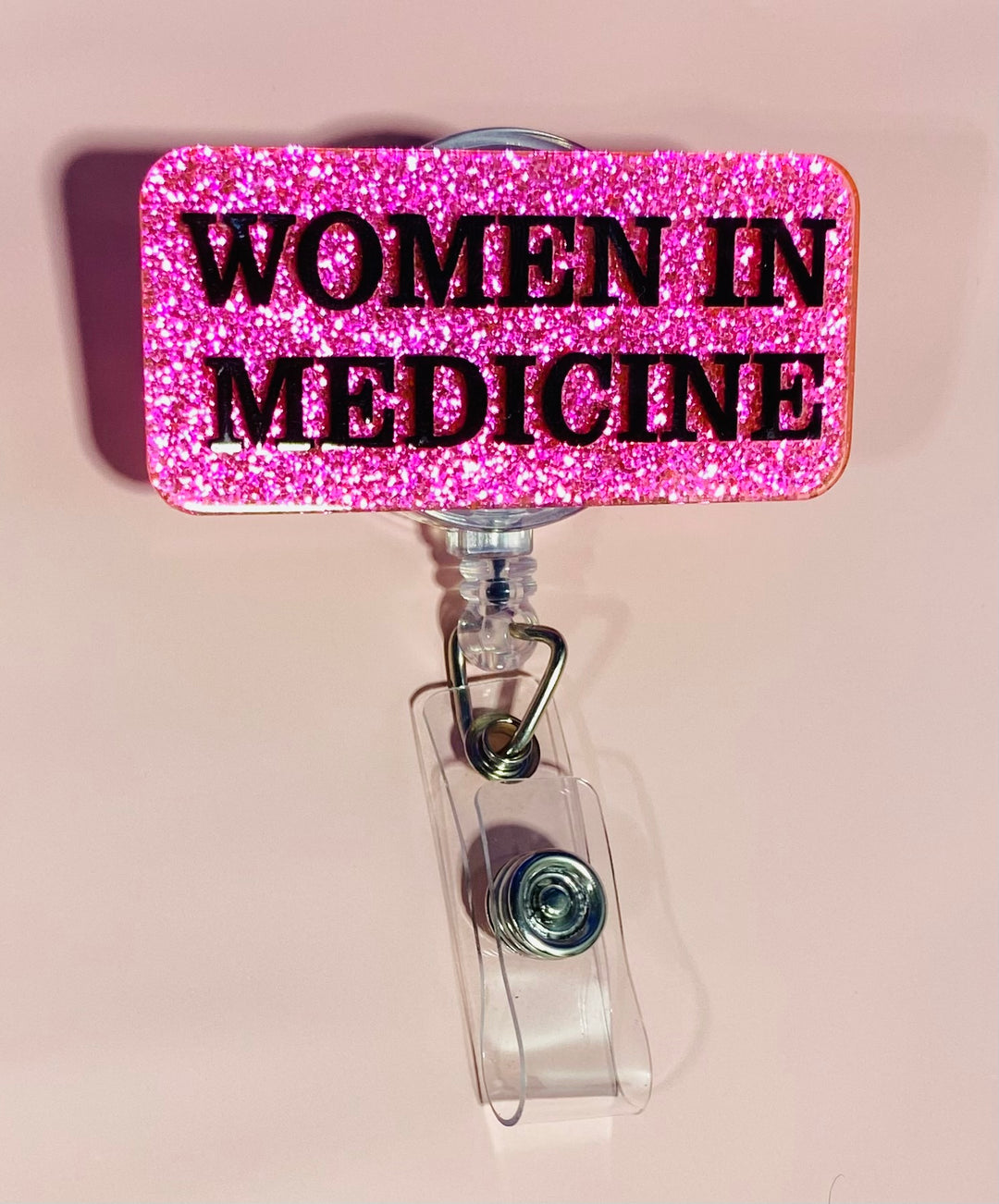 Pink glitter badge holder with 'WOMEN IN MEDICINE' text on a beige background